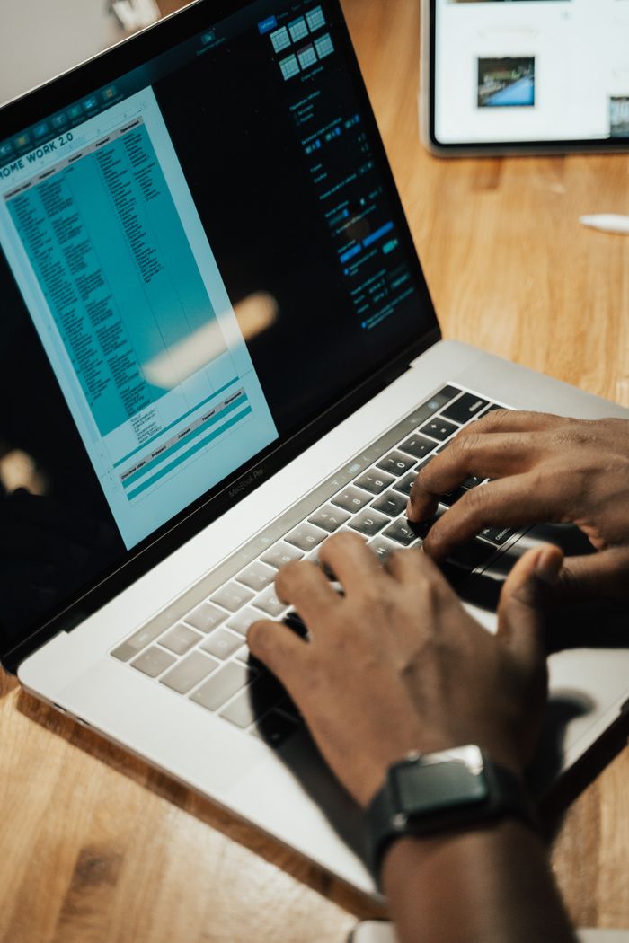 Close-up of hands typing on a laptop at a wooden table, focused on work at home.
