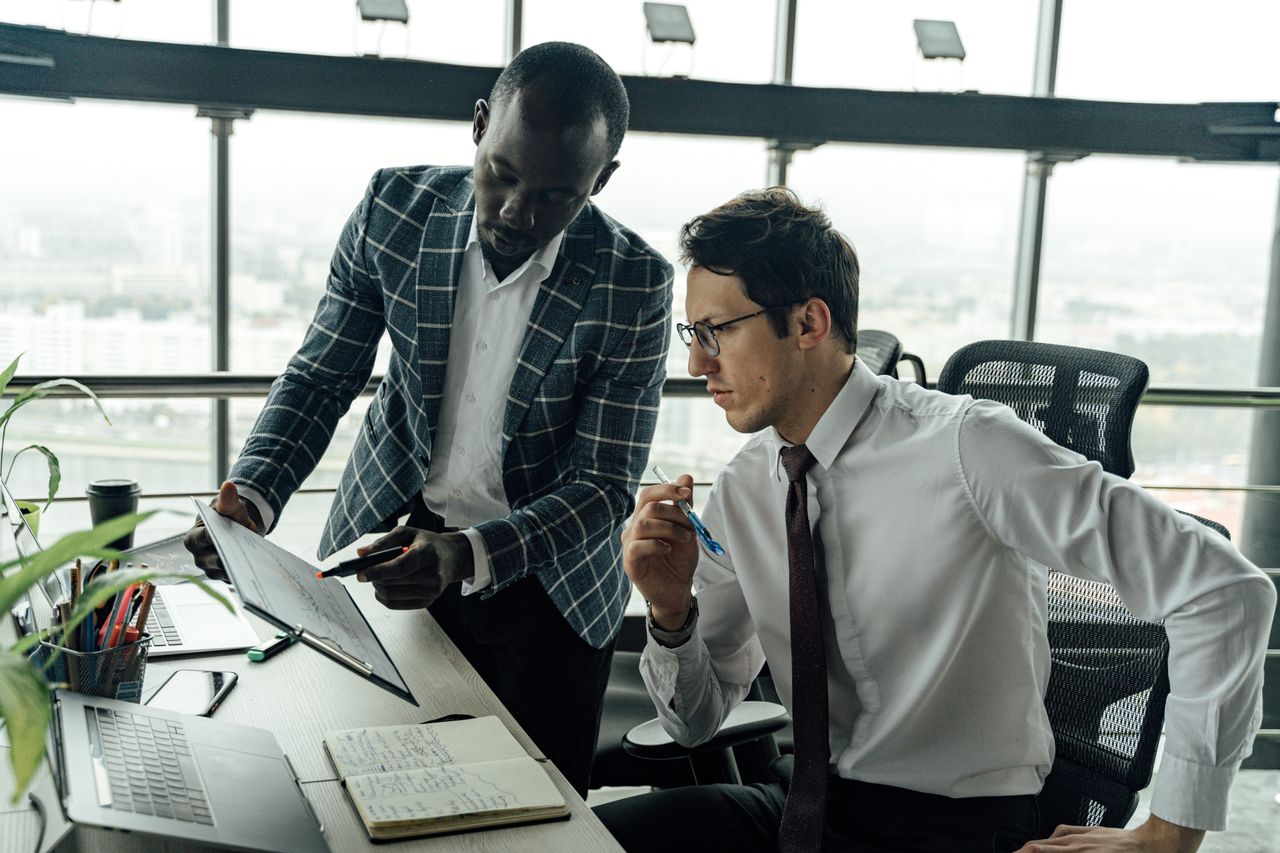Two businessmen collaborate in a modern office setting, engaged in a focused discussion.